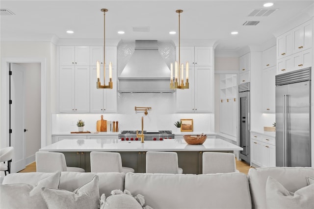 kitchen with pendant lighting, custom range hood, built in fridge, and white cabinets