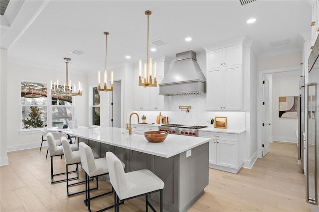 kitchen with a kitchen island with sink, white cabinetry, decorative light fixtures, and custom range hood