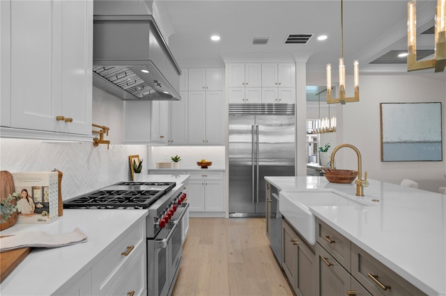 kitchen with premium range hood, sink, white cabinetry, hanging light fixtures, and high quality appliances