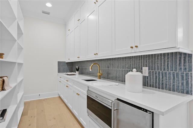 kitchen with sink, light wood-type flooring, ornamental molding, decorative backsplash, and white cabinets