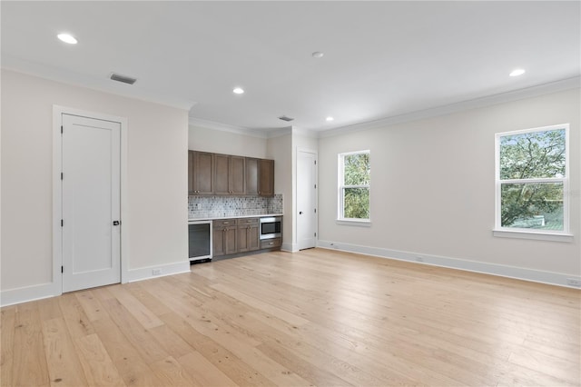 interior space featuring stainless steel microwave, wine cooler, decorative backsplash, crown molding, and light hardwood / wood-style flooring