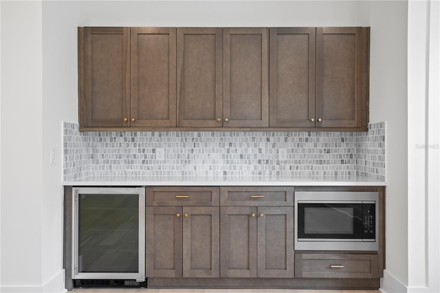 kitchen featuring wine cooler, dark brown cabinets, stainless steel microwave, and tasteful backsplash