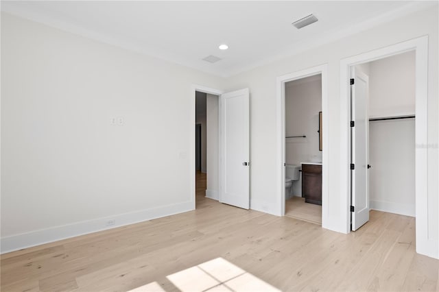 unfurnished bedroom with a closet, a walk in closet, ensuite bath, and light hardwood / wood-style flooring