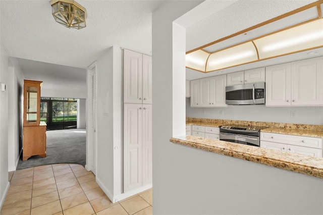 kitchen featuring white cabinets, light stone counters, a textured ceiling, stainless steel appliances, and light colored carpet