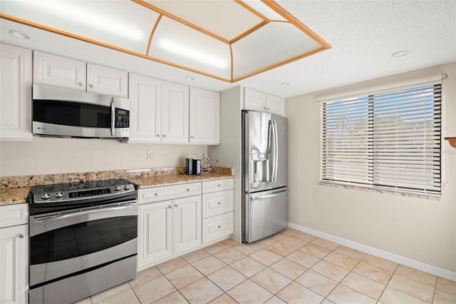 kitchen with light stone countertops, white cabinets, light tile patterned floors, appliances with stainless steel finishes, and a textured ceiling