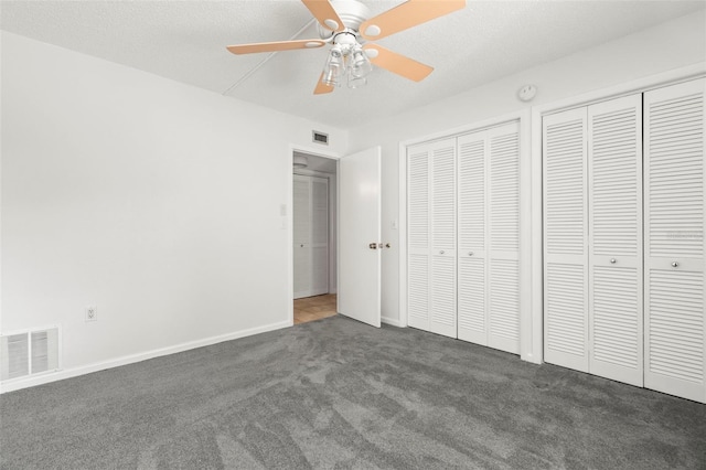 unfurnished bedroom with a textured ceiling, multiple closets, dark carpet, and ceiling fan