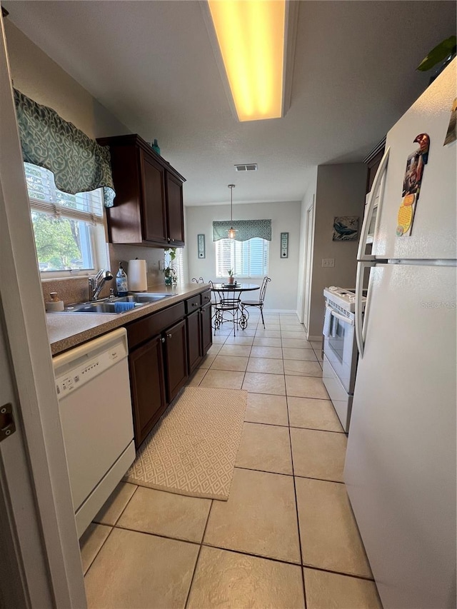 kitchen with hanging light fixtures, dark brown cabinets, light tile patterned flooring, sink, and white appliances