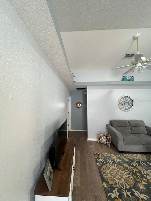 living room featuring a textured ceiling, dark wood-type flooring, and ceiling fan