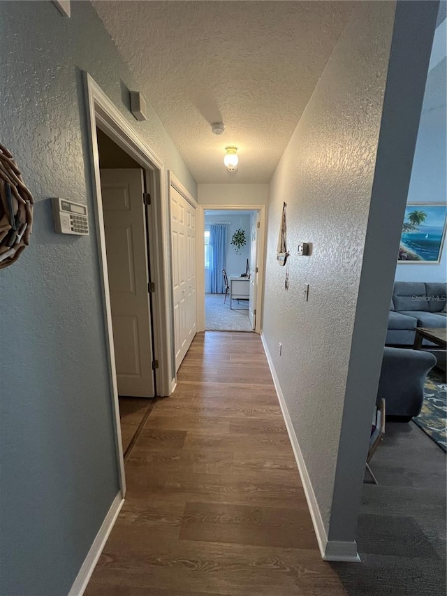 corridor with a textured ceiling and hardwood / wood-style floors