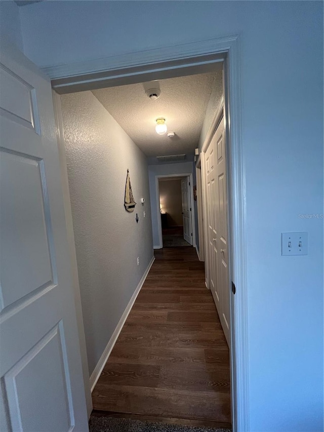 corridor featuring a textured ceiling and dark hardwood / wood-style flooring