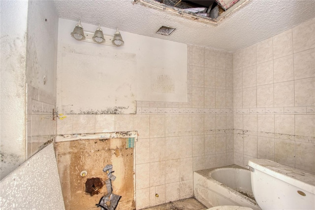 bathroom featuring a bath, toilet, a textured ceiling, and tile walls