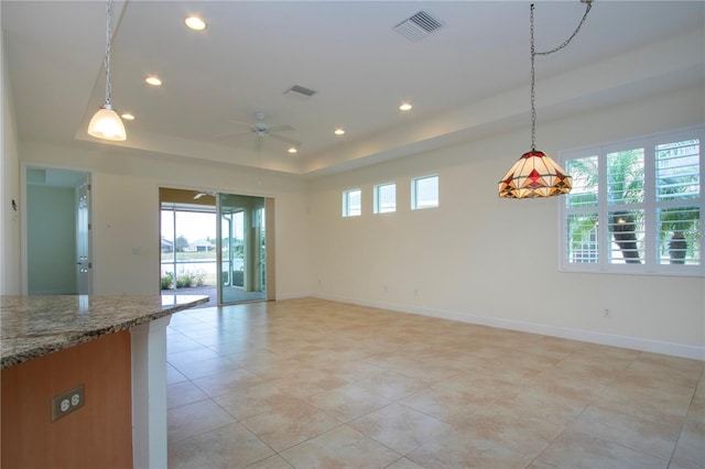 interior space with stone counters, hanging light fixtures, ceiling fan, and a tray ceiling