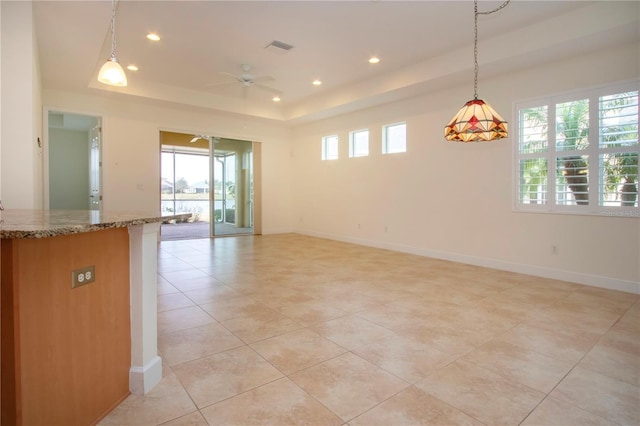 interior space featuring light stone counters, light tile patterned floors, a raised ceiling, pendant lighting, and ceiling fan