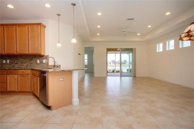 kitchen featuring decorative light fixtures, dishwasher, sink, a tray ceiling, and light stone countertops