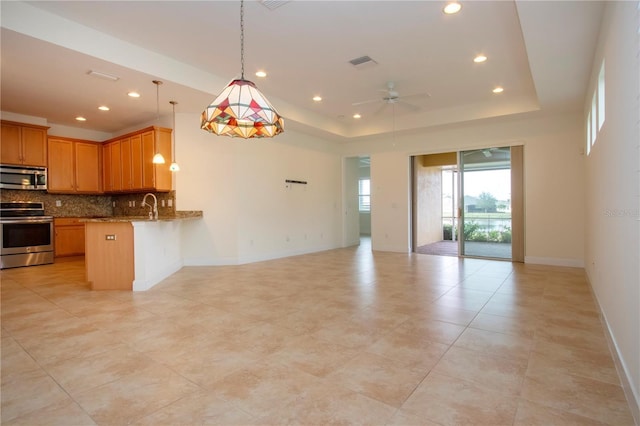 kitchen featuring appliances with stainless steel finishes, a tray ceiling, backsplash, hanging light fixtures, and kitchen peninsula