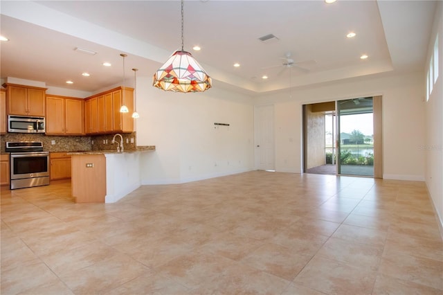 kitchen with stainless steel appliances, tasteful backsplash, light stone countertops, kitchen peninsula, and a raised ceiling