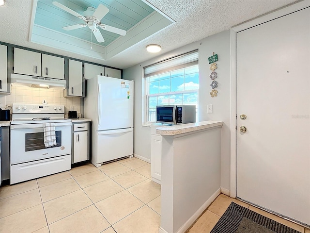 kitchen with light tile patterned flooring, backsplash, a textured ceiling, white appliances, and a tray ceiling