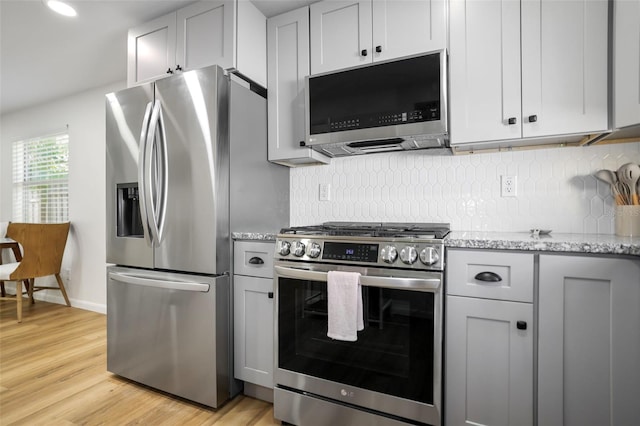 kitchen featuring decorative backsplash, appliances with stainless steel finishes, light stone countertops, light wood-type flooring, and gray cabinets