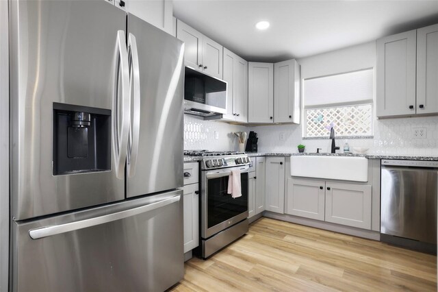 kitchen with light stone countertops, sink, light hardwood / wood-style floors, stainless steel appliances, and decorative backsplash