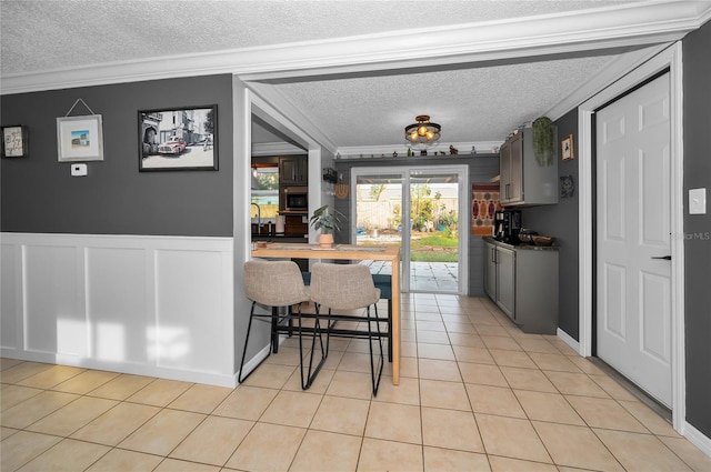 kitchen with ornamental molding, a kitchen bar, a textured ceiling, and light tile patterned floors