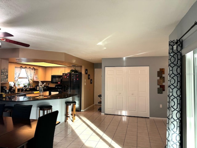 kitchen featuring black appliances, kitchen peninsula, a kitchen breakfast bar, a textured ceiling, and light tile patterned floors