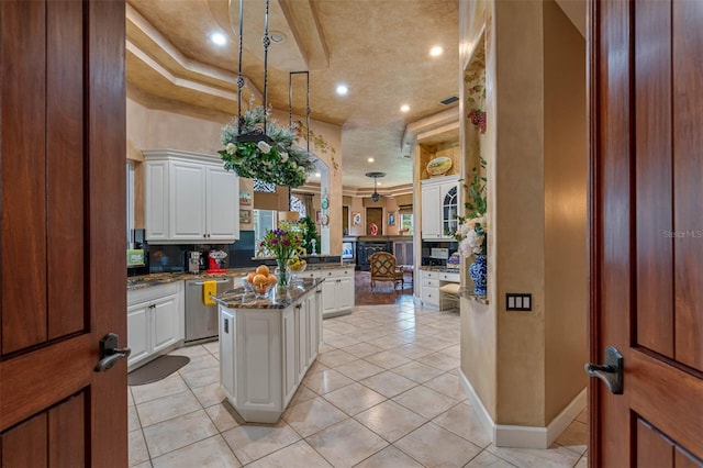 kitchen with a kitchen island, dark stone counters, pendant lighting, light tile patterned floors, and white cabinets