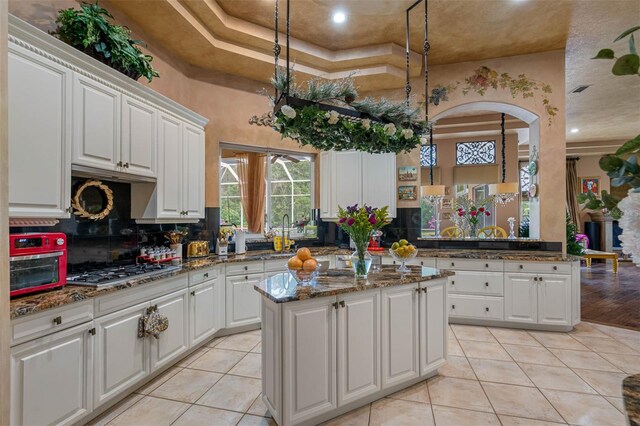 kitchen featuring stainless steel gas cooktop, white cabinets, dark stone counters, and a kitchen island