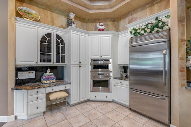 kitchen with light tile patterned flooring, white cabinets, stainless steel appliances, and dark stone counters