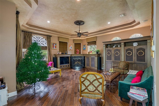 living area with dark wood-type flooring, plenty of natural light, and a raised ceiling