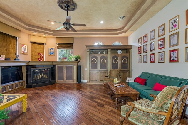 living room featuring hardwood / wood-style flooring, a raised ceiling, and ceiling fan