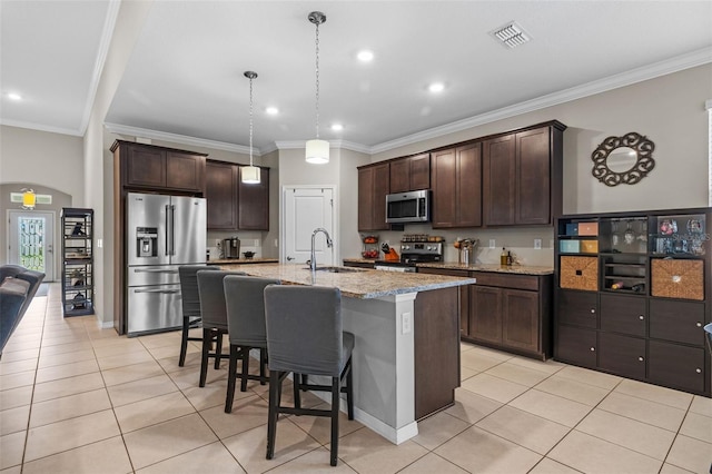 kitchen with a center island with sink, ornamental molding, appliances with stainless steel finishes, and light stone counters