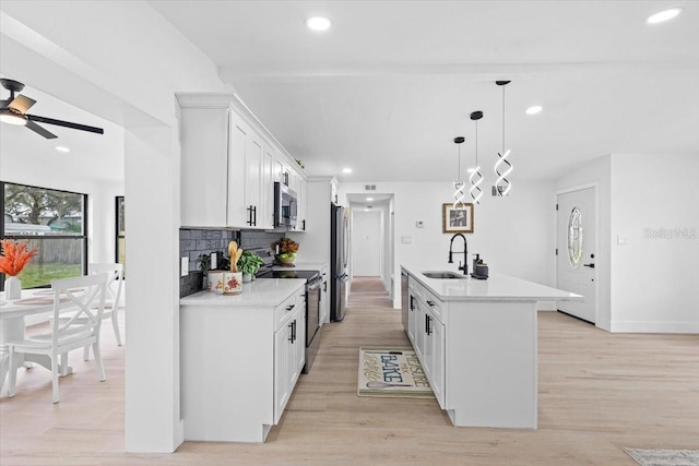 kitchen featuring white cabinets, a center island with sink, sink, appliances with stainless steel finishes, and decorative light fixtures