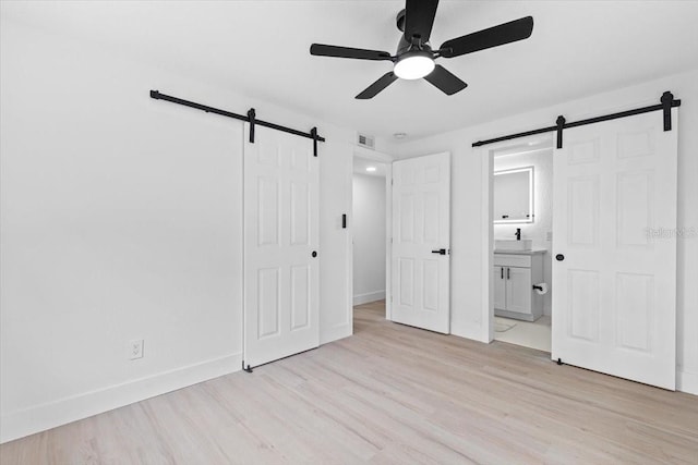 unfurnished bedroom featuring light wood-type flooring, connected bathroom, a barn door, and ceiling fan