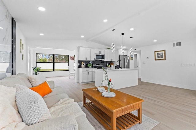 living room featuring light hardwood / wood-style flooring, lofted ceiling, and sink