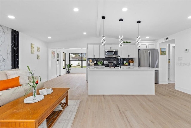 kitchen with pendant lighting, white cabinets, vaulted ceiling, tasteful backsplash, and stainless steel appliances