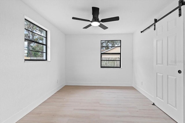 spare room with ceiling fan, a barn door, and light hardwood / wood-style flooring