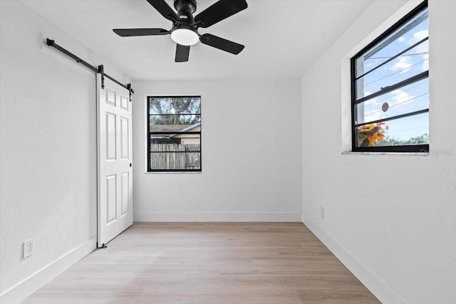 unfurnished bedroom featuring ceiling fan, a barn door, and light wood-type flooring