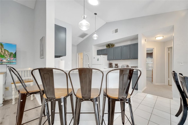 kitchen featuring white refrigerator, vaulted ceiling, decorative light fixtures, light tile patterned floors, and gray cabinets