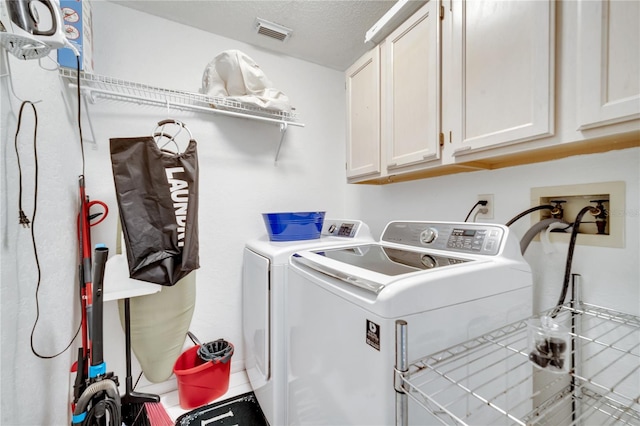 washroom with cabinets, washer and dryer, and a textured ceiling