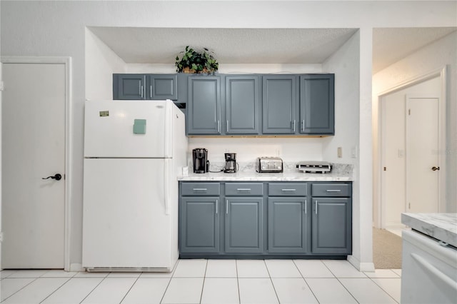 kitchen featuring gray cabinetry, light stone countertops, light tile patterned flooring, a textured ceiling, and white fridge