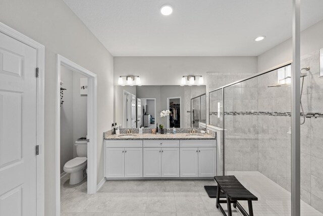 bathroom featuring toilet, vanity, a tile shower, and tile patterned flooring