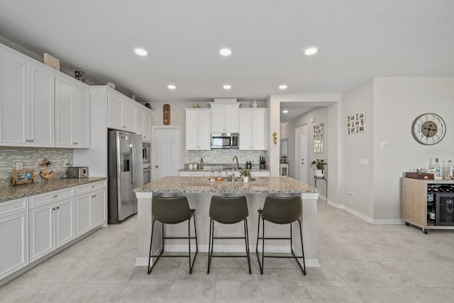 kitchen featuring white cabinetry, stainless steel appliances, light stone counters, and a center island with sink