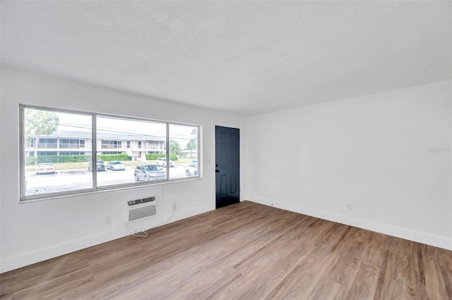 spare room featuring an AC wall unit, light hardwood / wood-style floors, and a textured ceiling