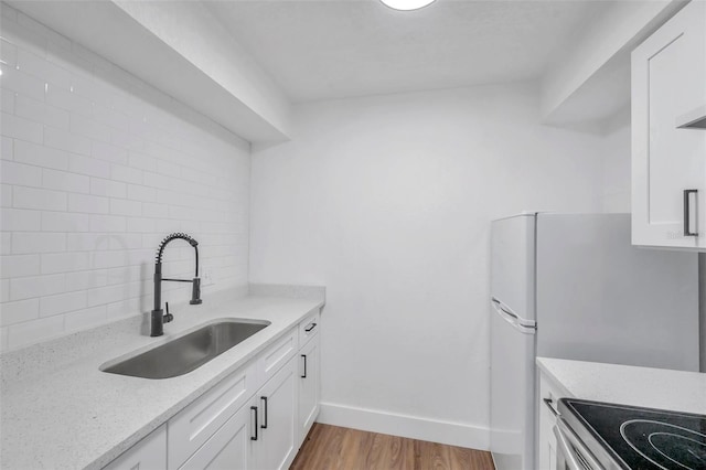 kitchen with light stone countertops, light wood-type flooring, sink, white fridge, and white cabinetry