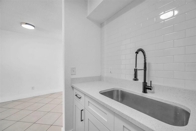 kitchen with light stone counters, white cabinetry, sink, and light tile patterned floors