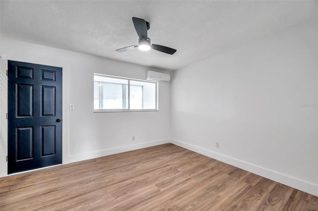 spare room with a wall unit AC, ceiling fan, a textured ceiling, and light wood-type flooring