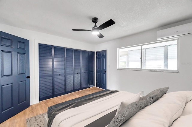 bedroom with an AC wall unit, ceiling fan, hardwood / wood-style floors, and a textured ceiling