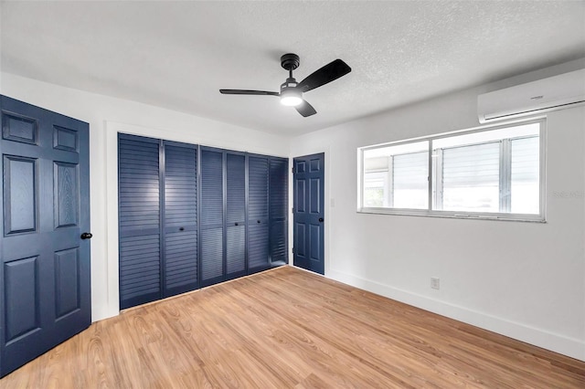 unfurnished bedroom with ceiling fan, wood-type flooring, a textured ceiling, and a wall mounted AC