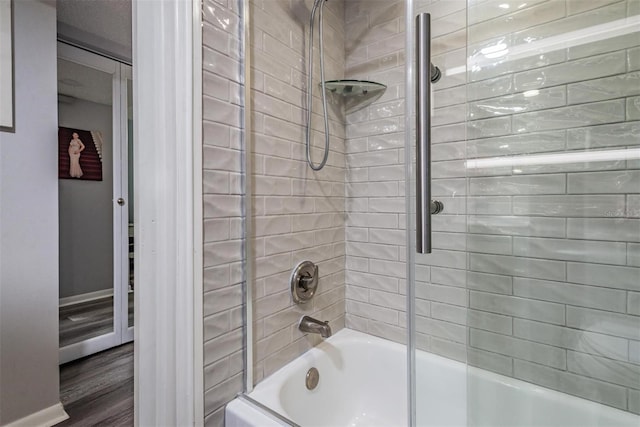 bathroom with a textured ceiling, enclosed tub / shower combo, and hardwood / wood-style flooring