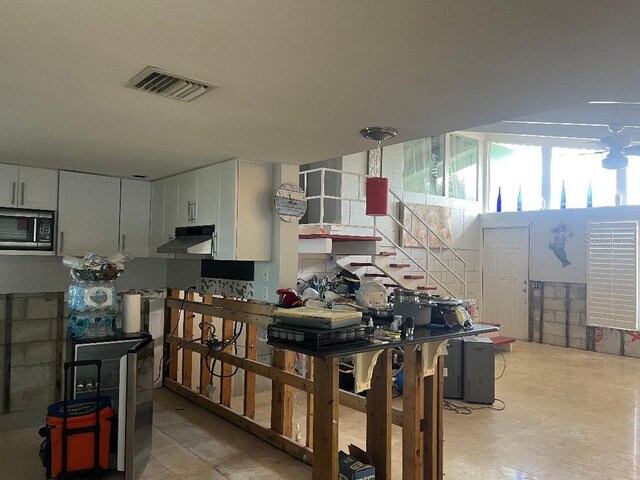 interior space with under cabinet range hood, visible vents, white cabinets, and stainless steel microwave